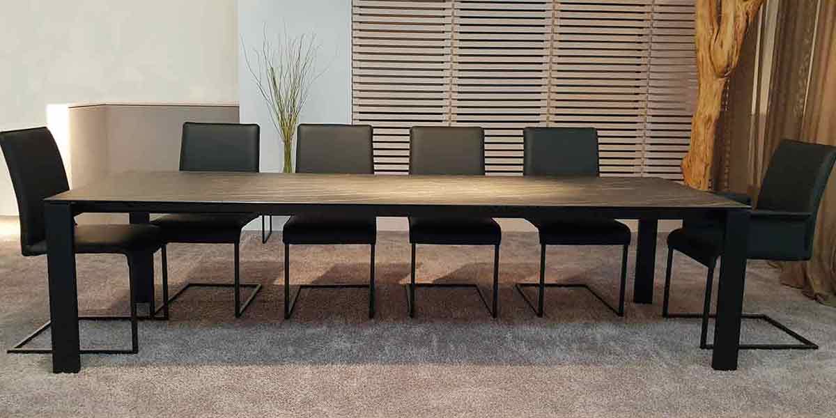 Kategorie Banner Stühle Sechs Stühle an einem langen Esstisch platziert im Showroom Ronald Schmitt. Freischwinger mit braunem Lederbezug.