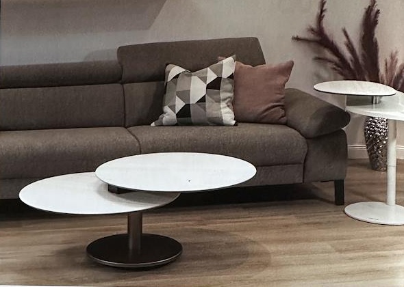 Couchtisch mit zwei runden, drehbaren Tischplatten aus hellem Stein-Dekor vor einem grauen Sofa, daneben ein passender Beistelltisch.